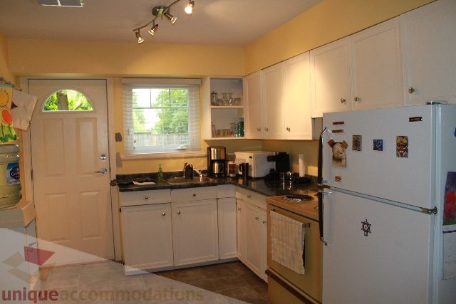 Bright kitchen with white cabinets, stainless steel appliances, and a window with a view of greenery. - 2730 Ailsa Crescent, North Vancouver