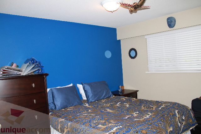 Bedroom with blue walls, patterned bedspread, and window with blinds. - 2730 Ailsa Crescent, North Vancouver