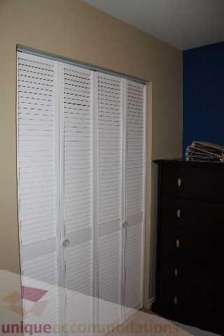 Bedroom with white louvered closet doors and dark wood dresser. - 2730 Ailsa Crescent, North Vancouver