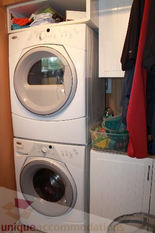 Laundry room with stacked washer and dryer, white cabinets, and hanging clothes. - 2730 Ailsa Crescent, North Vancouver