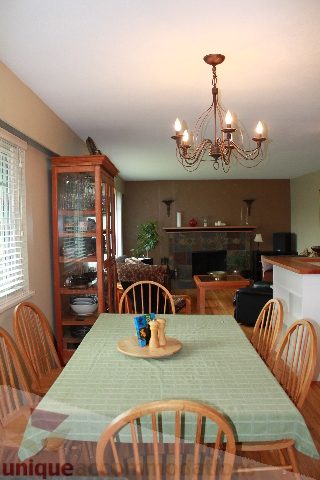 Dining area with wooden chairs, green tablecloth, chandelier, and kitchen in background. - 2730 Ailsa Crescent, North Vancouver