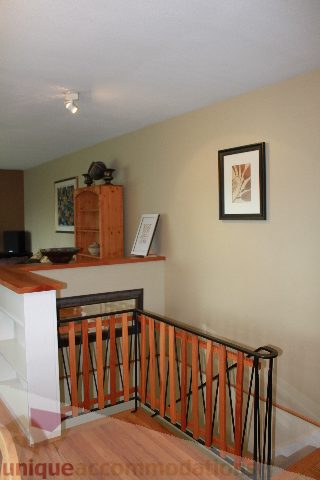 Framed artwork decorates the wall above a wooden countertop, with a staircase railing in the foreground. - 2730 Ailsa Crescent, North Vancouver