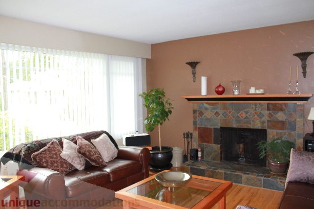 Furnished living room with stone fireplace, hardwood floors, and large windows. - 2730 Ailsa Crescent, North Vancouver