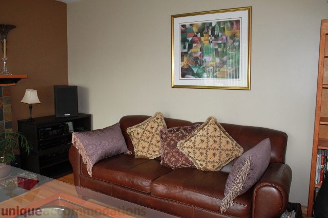 Furnished living room with leather couch, framed art, and entertainment center. - 2730 Ailsa Crescent, North Vancouver