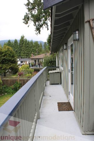 Balcony with wooden railings, greenery, and distant mountain view. - 2730 Ailsa Crescent, North Vancouver