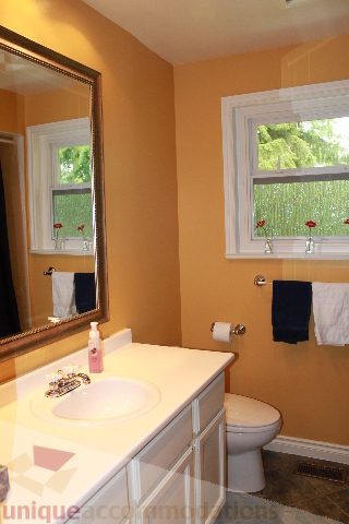 Bathroom with yellow walls, white countertop, and window view of greenery. - 2730 Ailsa Crescent, North Vancouver