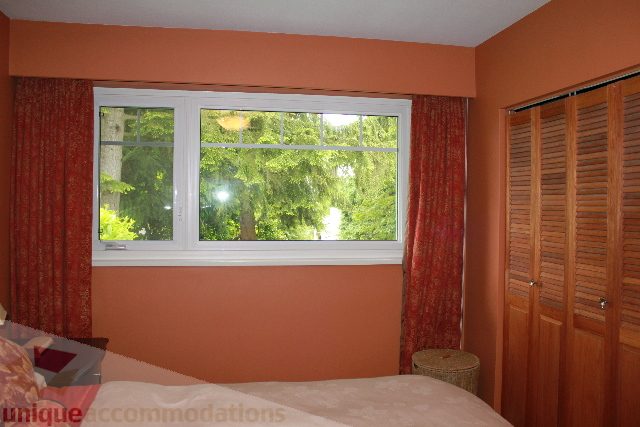 Bright living room with orange walls, large window with red curtains, and wooden shutters. - 2730 Ailsa Crescent, North Vancouver