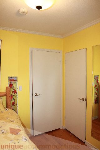Bright bedroom with yellow walls, wooden floors, and a white door. - 2730 Ailsa Crescent, North Vancouver