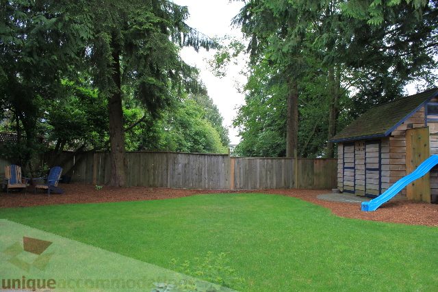 Fenced backyard with wooden playhouse and slide, surrounded by tall trees. - 2730 Ailsa Crescent, North Vancouver