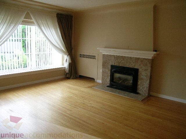 Bright living room with hardwood floors and a fireplace, large window with curtains. - 1561 Jefferson Ave, West Vancouver