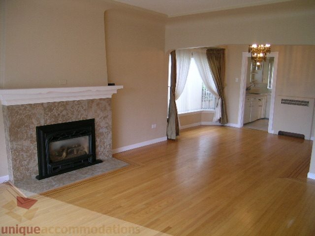 Bright living room with hardwood floors, fireplace, and view of another room. - 1561 Jefferson Ave, West Vancouver