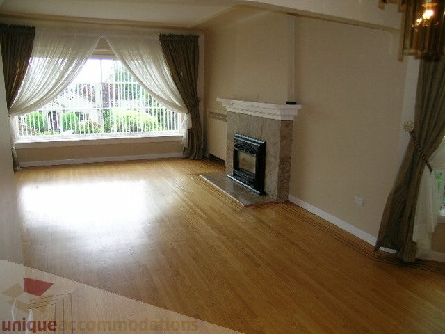 Bright living room with hardwood floors and a fireplace, featuring a large window with a city view. - 1561 Jefferson Ave, West Vancouver