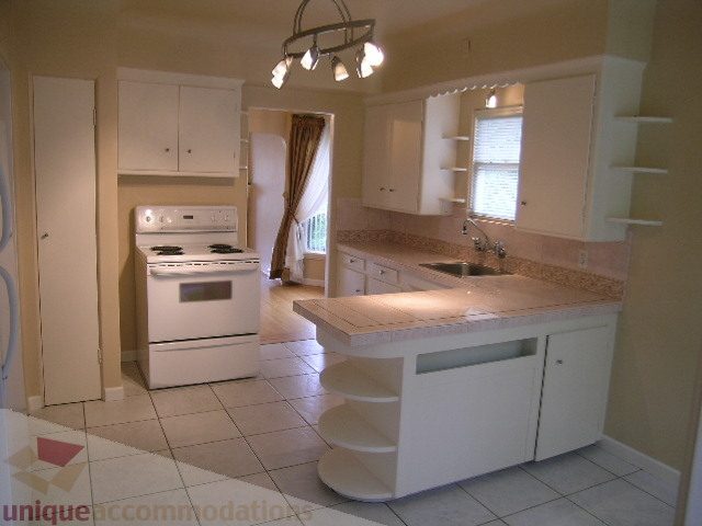 Bright kitchen with white cabinets, granite countertops, and a tiled floor. - 1561 Jefferson Ave, West Vancouver