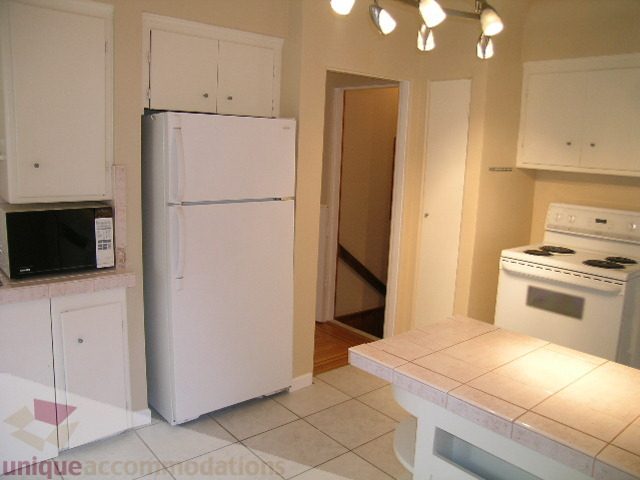 Bright kitchen with white cabinets, tiled countertops, and a white refrigerator. - 1561 Jefferson Ave, West Vancouver