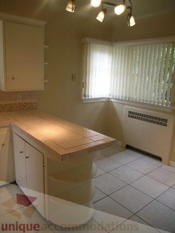 Bright kitchen with tiled countertops and white cabinets, natural light from window. - 1561 Jefferson Ave, West Vancouver