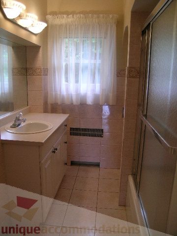 Bright bathroom with white sink, tiled floor, and sliding glass shower door. - 1561 Jefferson Ave, West Vancouver