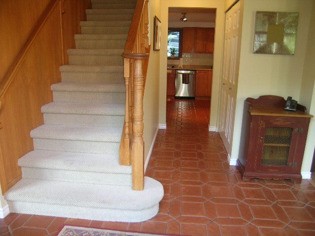 Staircase leading to kitchen with stainless steel appliances and terracotta tiled floor. - 5753 Westport Road, West Vancouver