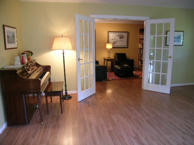 Living room with hardwood floors, piano, and French doors leading to another room. - 5753 Westport Road, West Vancouver