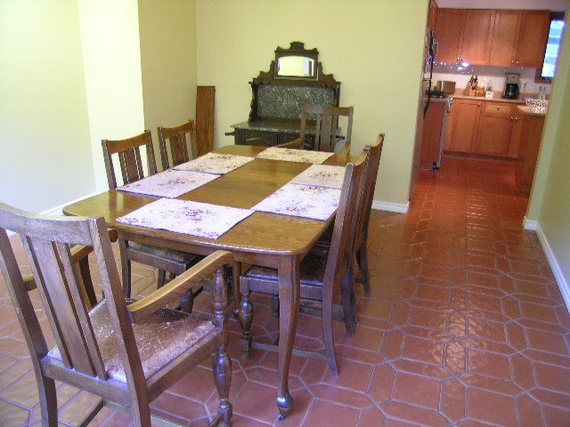 Bright dining area with hexagonal terracotta floor, wooden chairs, and a dark stone fireplace. - 5753 Westport Road, West Vancouver