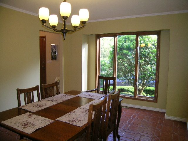 Dining room with wooden table, floral placemats, and large windows showing greenery. - 5753 Westport Road, West Vancouver