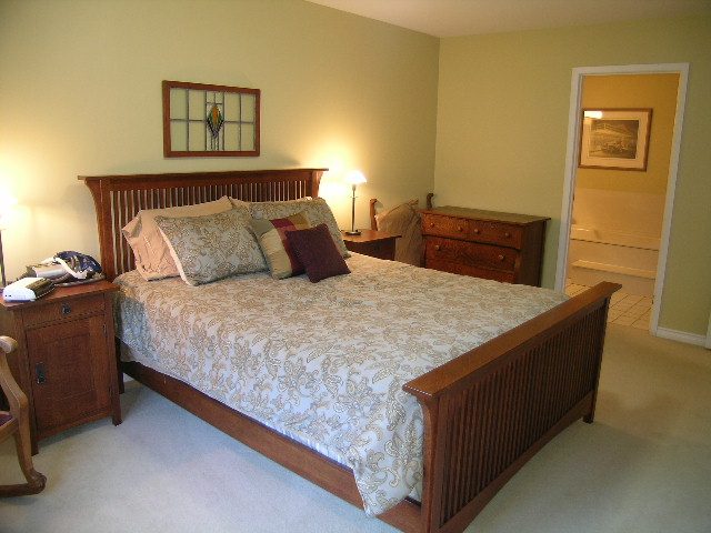 Spacious bedroom with wooden bed frame and patterned bedding, featuring a nightstand and dresser. - 5753 Westport Road, West Vancouver