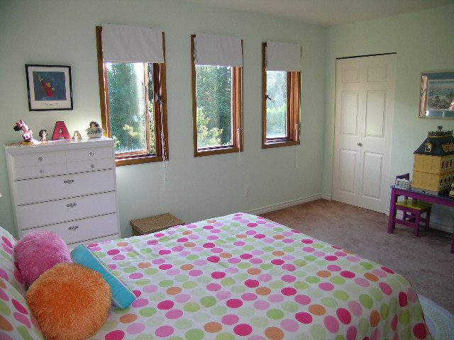 Bright bedroom with colorful bedding, wooden floors, and a view of greenery outside. - 5753 Westport Road, West Vancouver