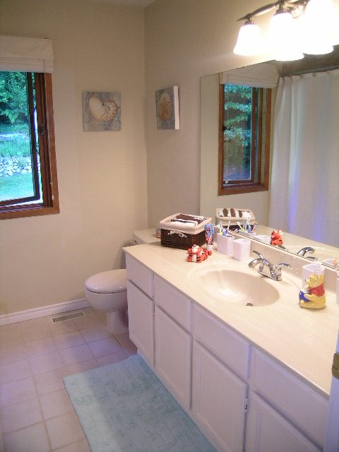 Bright bathroom with white cabinets, countertop, and a window view. - 5753 Westport Road, West Vancouver