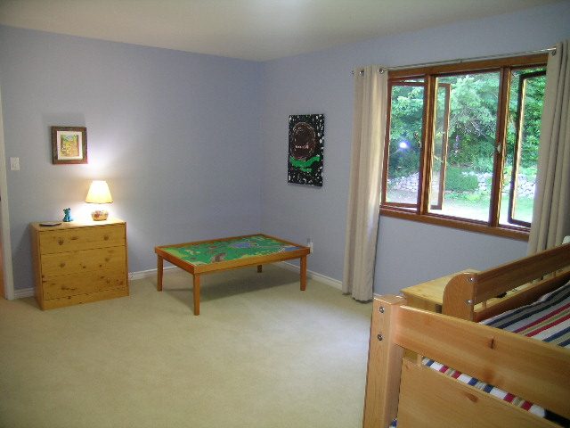 Bright bedroom with twin beds, light blue walls, and sliding glass doors leading to a garden view. - 5753 Westport Road, West Vancouver