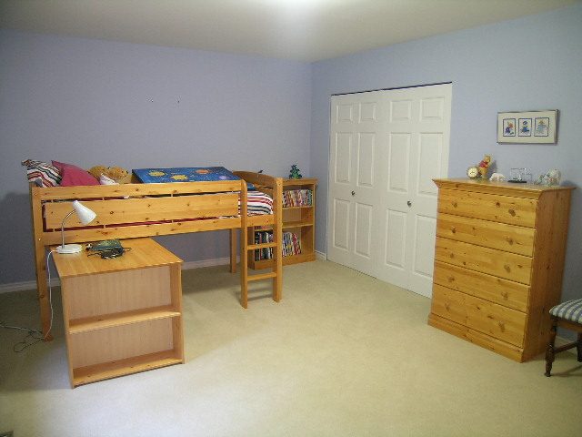 Bright bedroom with wooden furniture, light blue walls, and a door. - 5753 Westport Road, West Vancouver