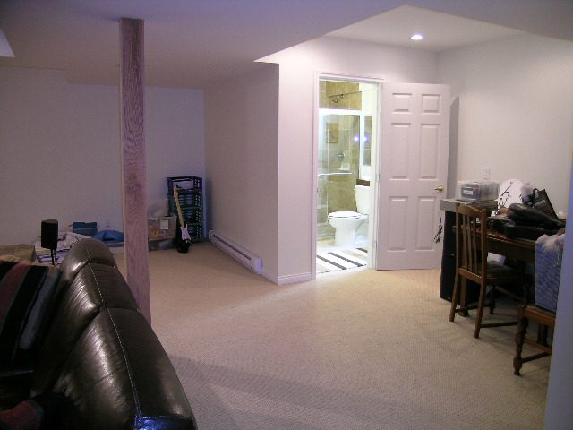 Living room with leather couch and carpeted floor, leading to a kitchen area. - 5753 Westport Road, West Vancouver