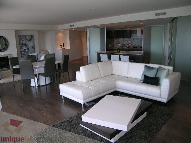 Modern living room with white sectional sofa, hardwood floors, and kitchen in the background. - 3306 - 1011 West Cordova Street, Vancouver Downtown