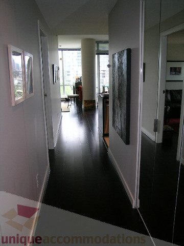 Furnished hallway with dark flooring and framed artwork, leading to a living area with a city view. - 707 - 638 Beach Crescent, Vancouver Downtown