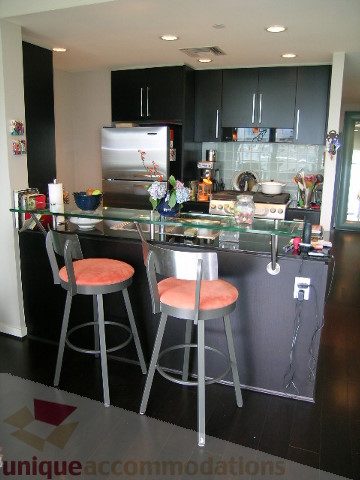 Bright kitchen with modern black cabinetry, glass countertops, and orange bar stools. - 707 - 638 Beach Crescent, Vancouver Downtown