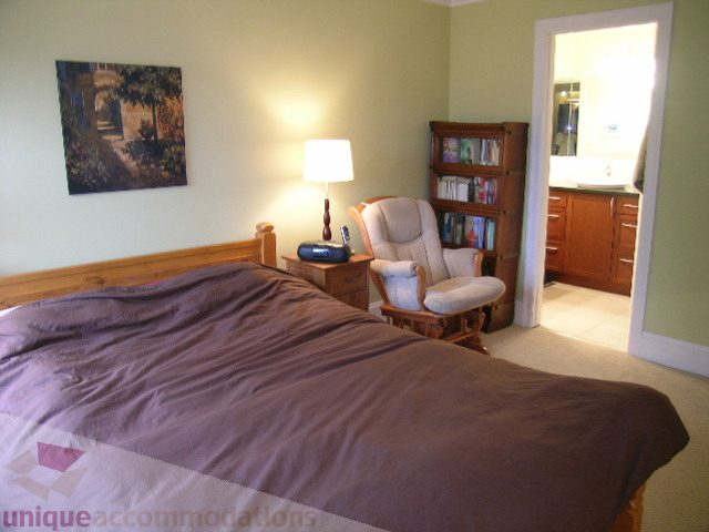 Bright bedroom with hardwood floors, cozy seating, and a view of the bathroom. - 405 - 4001 Mount Seymour Pkwy, North Vancouver
