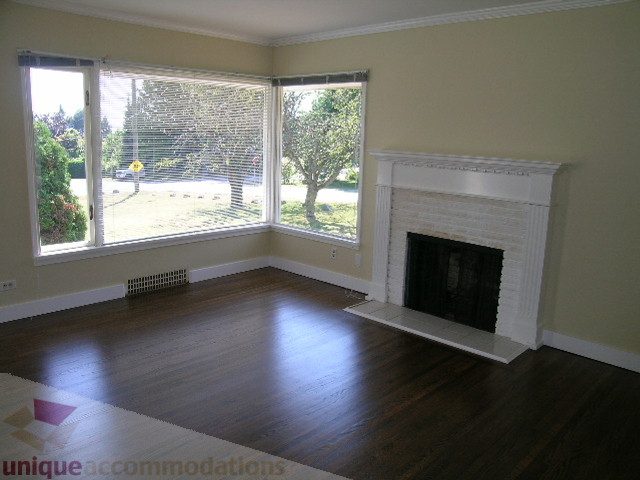Spacious living room with hardwood floors, large windows, and a fireplace. - 1350 14th Street, West Vancouver