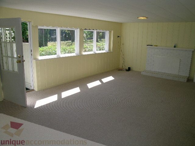 Bright sunlit living room with large windows, carpeted floor, and white fireplace. - 1350 14th Street, West Vancouver