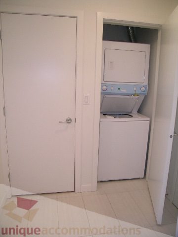 Bright laundry room with stacked washer and dryer, white walls, and tiled floor. - 406 - 1252 Hornby Street, Vancouver Downtown