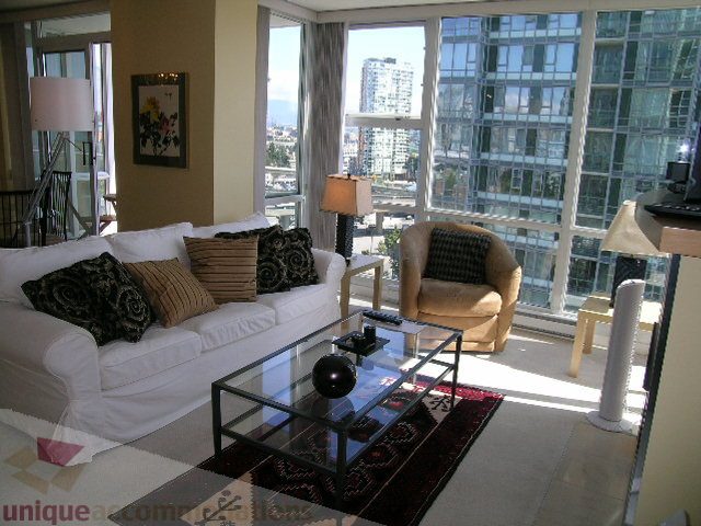 Bright living room with large windows offering a stunning city view, modern furniture, and a glass coffee table.