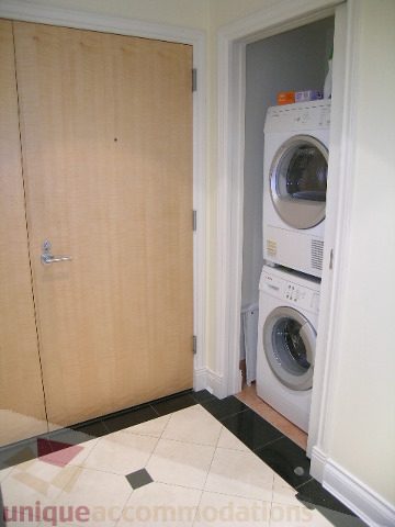 Furnished laundry room with stacked washer and dryer, tiled floor, and wooden door. - 1602 - 560 Cardero, Vancouver Downtown