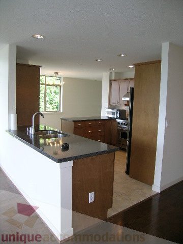 Modern kitchen with granite countertops and hardwood floors, featuring a city view through the window. - 8601 Seascape Place, West Vancouver