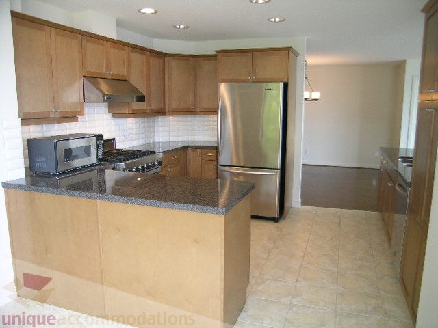 Modern kitchen with granite countertops, stainless steel appliances, and light wood cabinets. - 8601 Seascape Place, West Vancouver