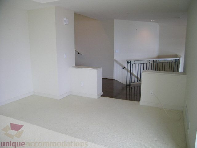 Spacious living room with white walls, carpeted floors, and a staircase leading to the upper level. - 8601 Seascape Place, West Vancouver