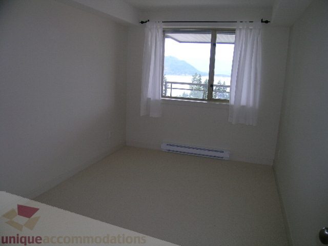 Spacious bedroom with a serene view of the mountains and water, featuring white walls and a cozy corner. - 8601 Seascape Place, West Vancouver
