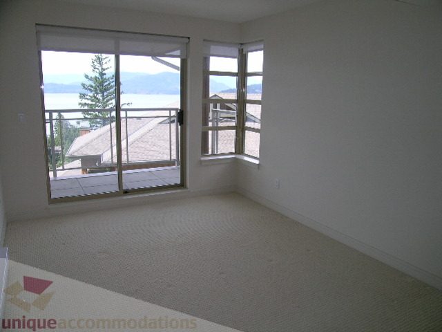 Spacious bedroom with large windows offering a serene view of the water and mountains. - 8601 Seascape Place, West Vancouver
