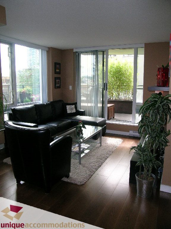Bright living room with hardwood floors, black leather furniture, and sliding glass doors leading to a balcony.