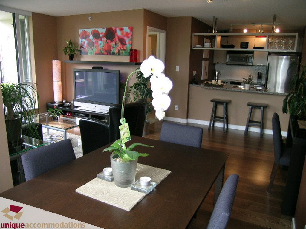 Furnished dining area with hardwood floors and modern decor, open to a kitchen with stainless steel appliances and city view.