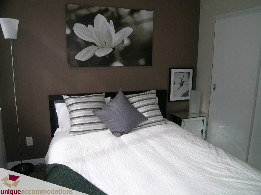 Furnished bedroom with white bedding, striped pillows, and a large floral artwork on the wall. - 316 - 1082 Seymour, Vancouver Downtown