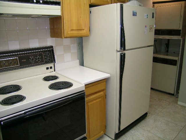 Bright kitchen with white appliances, wooden cabinets, and tiled backsplash. - 108 - 1279 Nicola Street, Vancouver Downtown