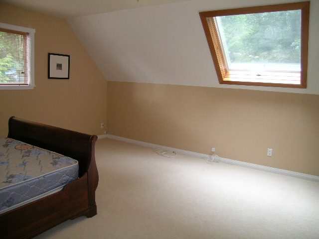 Bright attic bedroom with sloped ceiling and skylight, featuring a wooden bed frame and carpeted floor. - 992 Canyon Blvd, North Vancouver