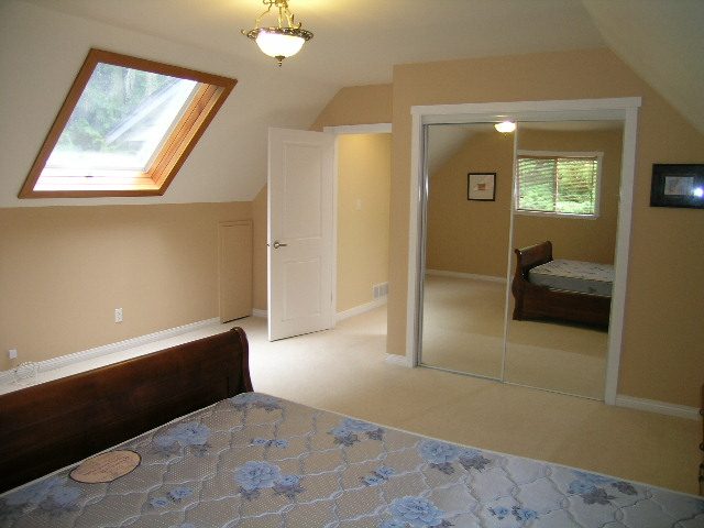 Bright attic bedroom with skylight, wooden headboard, and floral mattress. - 992 Canyon Blvd, North Vancouver